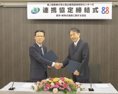 国立循環器病研究センターと森ノ宮医療大学の連携に関する協定締結式で、協定書を手にした2名の理事長が握手をしている様子。